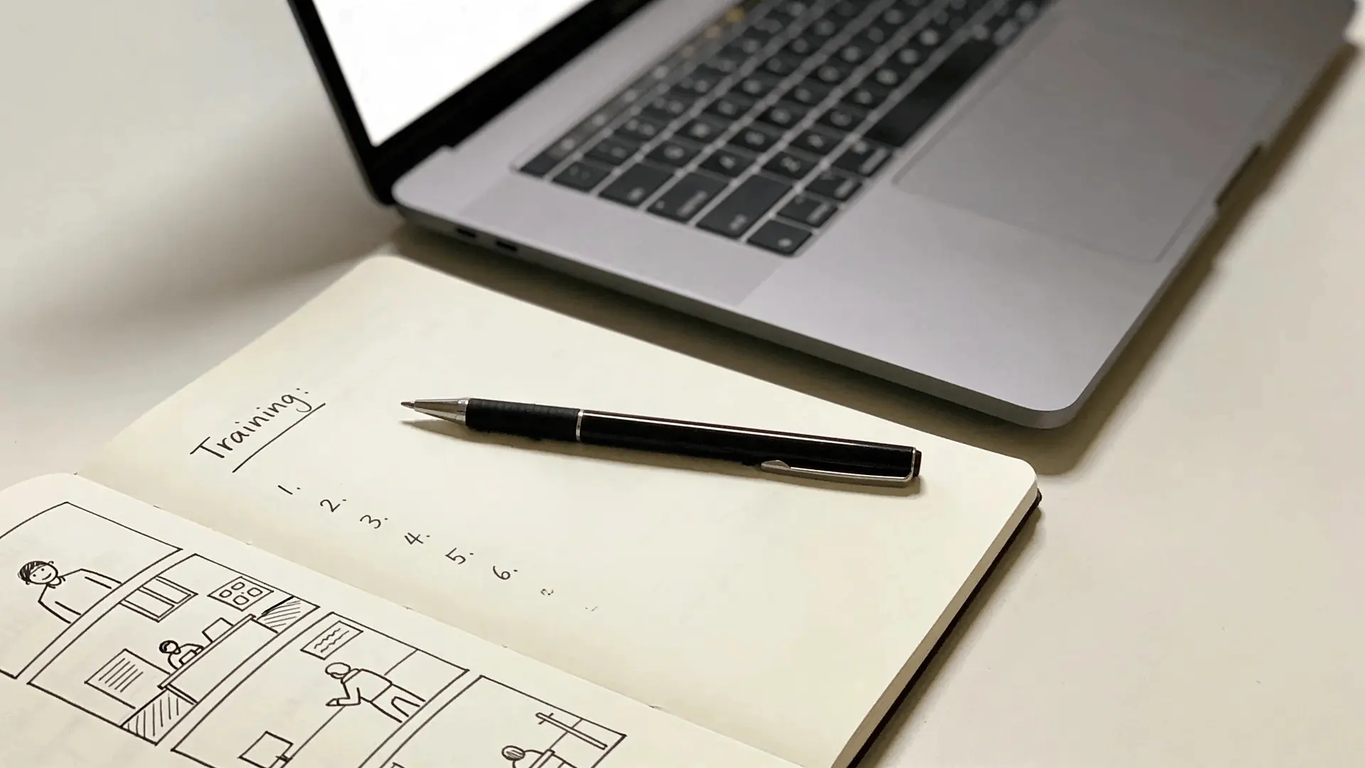 Notebook with storyboard sketches and training outline placed beside a laptop on a desk