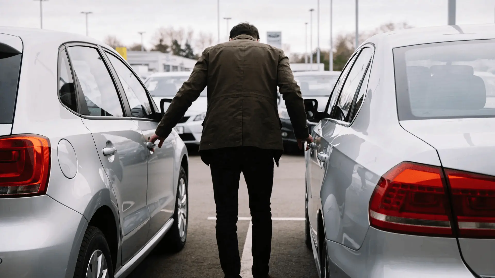 Person standing between two parked cars comparing vehicles in a dealership lot