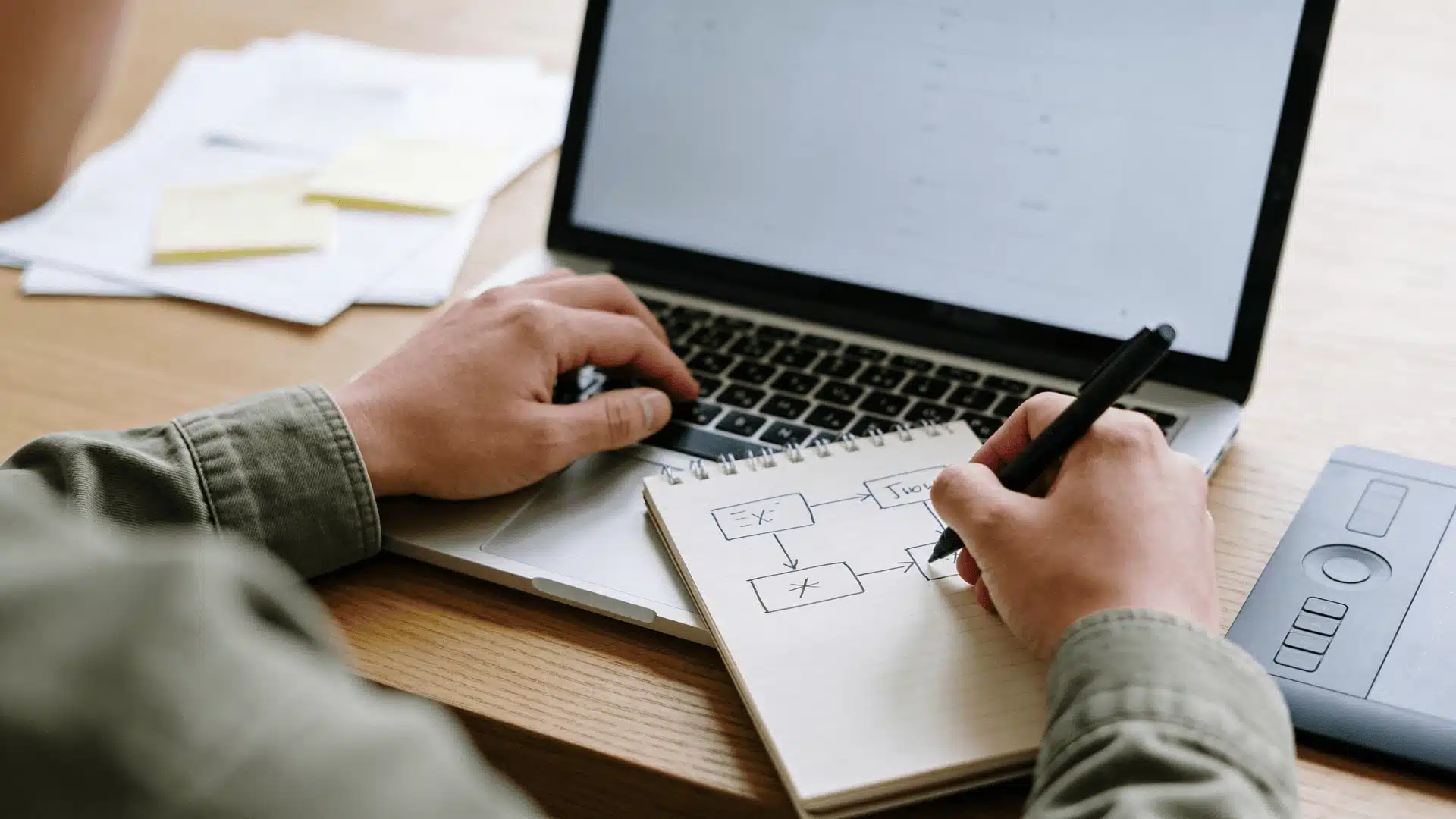 Person using a laptop with a notebook showing a simple workflow on a clean desk