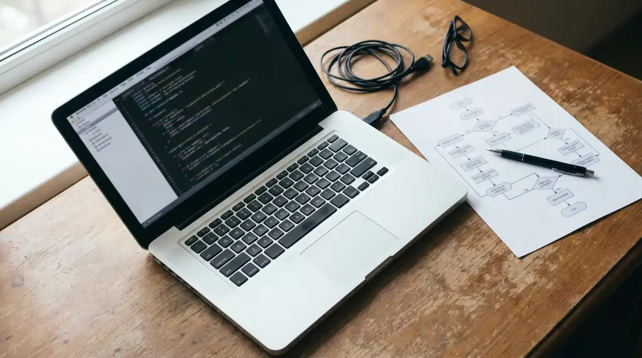 Printed document beside an open laptop with a code file and a sticky note between them
