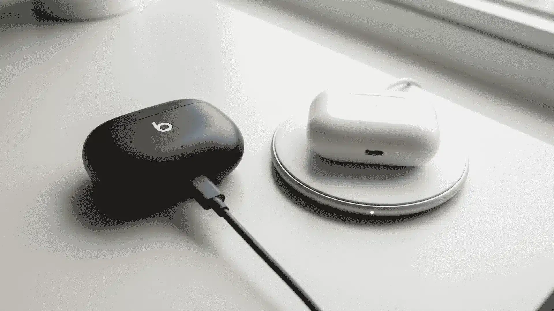 Earbud case charging via USB-C cable beside a case on a wireless charging pad