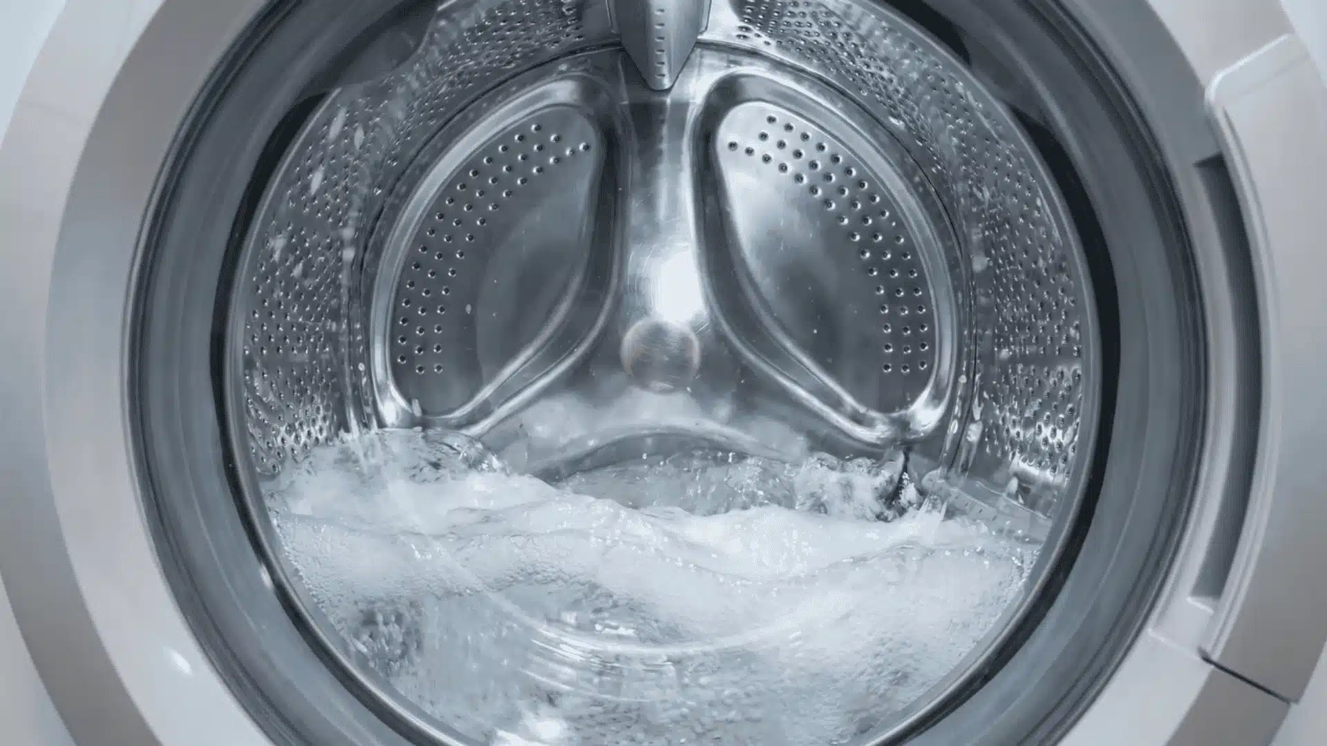 Empty stainless steel washer drum with water moving during a cleaning cycle