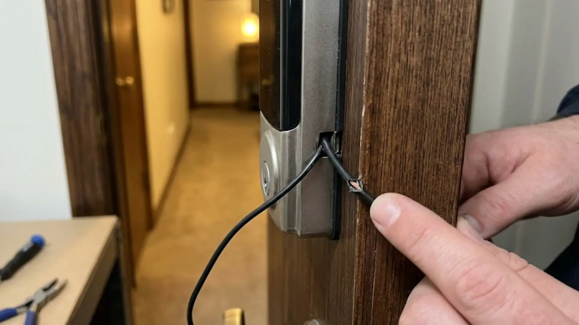hand pointing to a pinched, damaged wire on a newly installed smart lock on a wood door