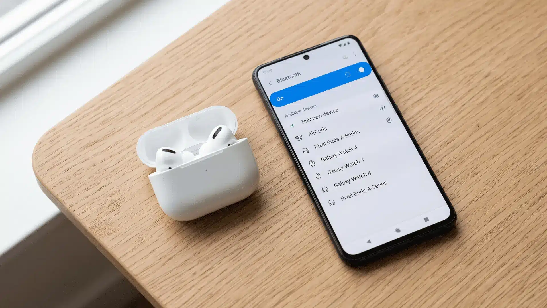 AirPods in an open charging case beside an Android phone displaying Bluetooth settings.