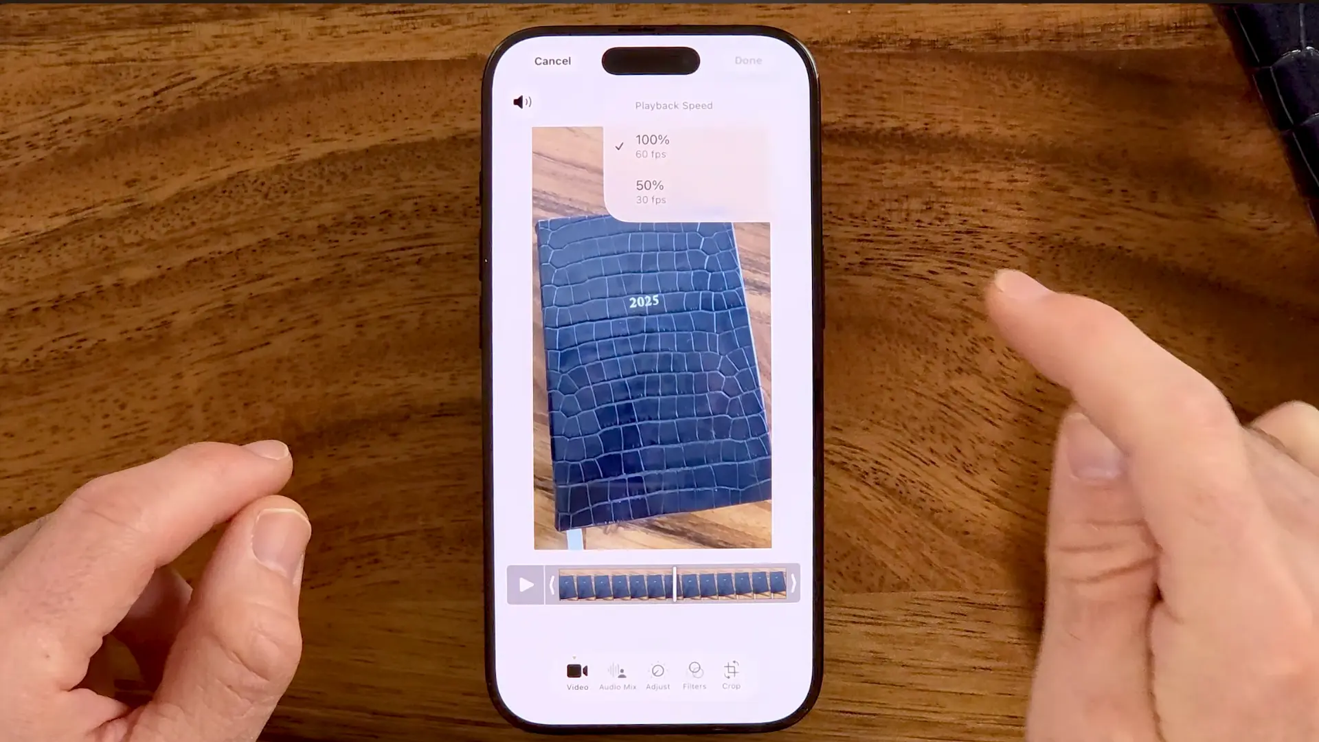 Hands holding a smartphone on a wooden table, displaying video playback speed options during video editing.