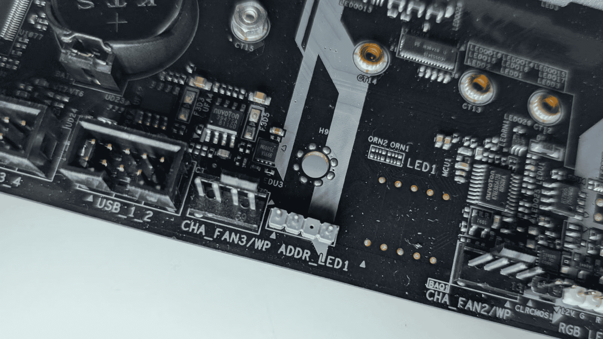 Close-up of a motherboard showing labeled internal headers for USB 1_2, chassis fans, and addressable RGB