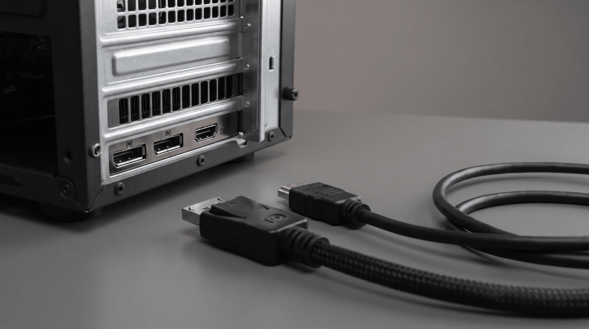 DisplayPort and HDMI ports on a graphics card rear panel with two cables resting on a desk surface