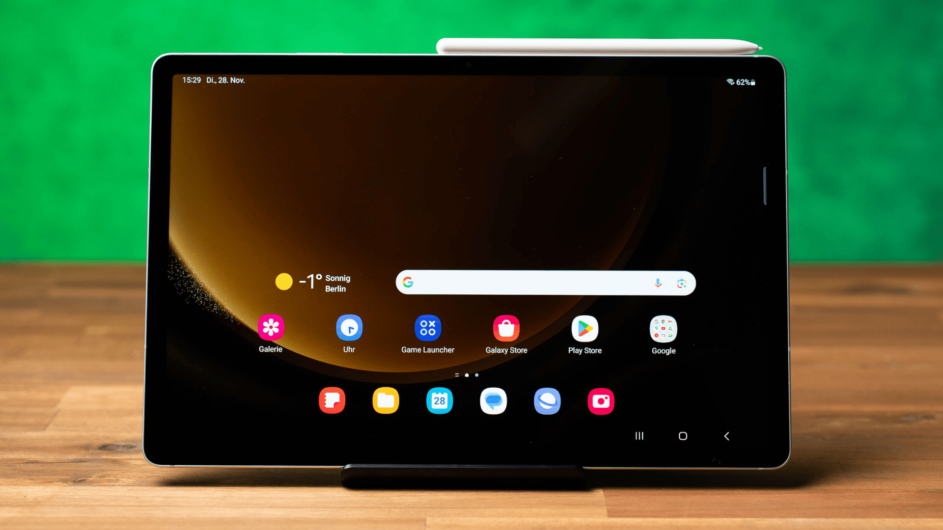 Front view of a Samsung Galaxy tablet resting on a wooden desk with a stylus attached to its top edge.