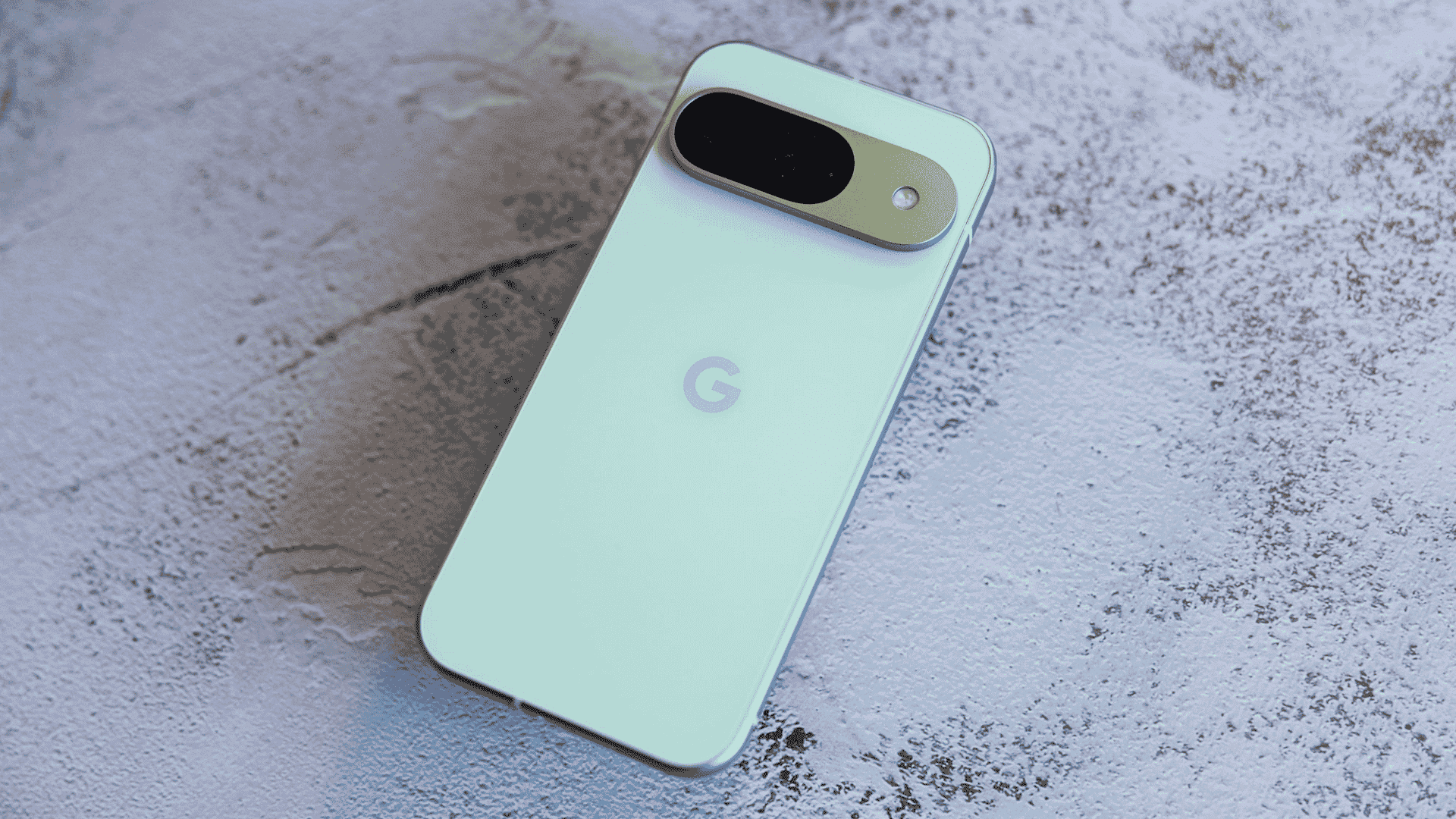 Back view of a light mint green Google Pixel 9 smartphone lying flat on a textured concrete surface.