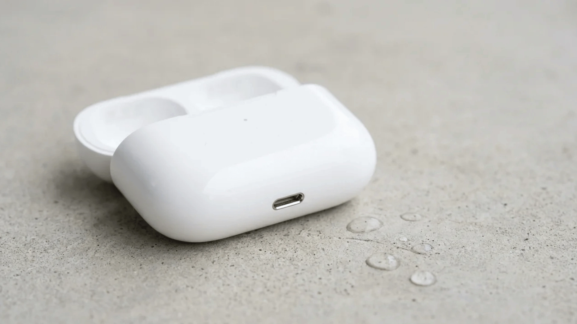 Open AirPods Pro charging case on a dry surface with water droplets nearby.
