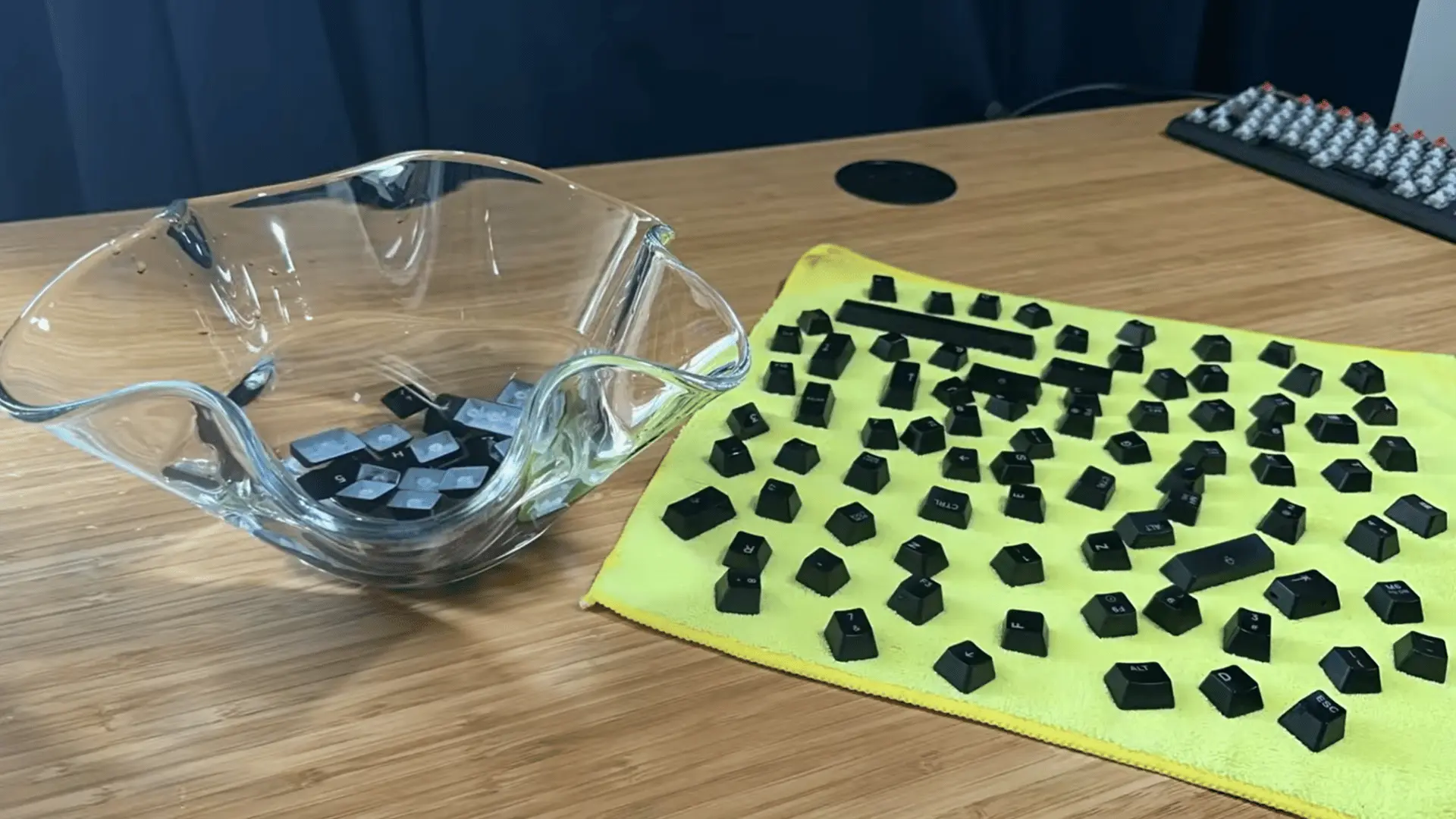 Keyboard keycaps removed and arranged on a cloth beside a glass bowl on a wooden desk