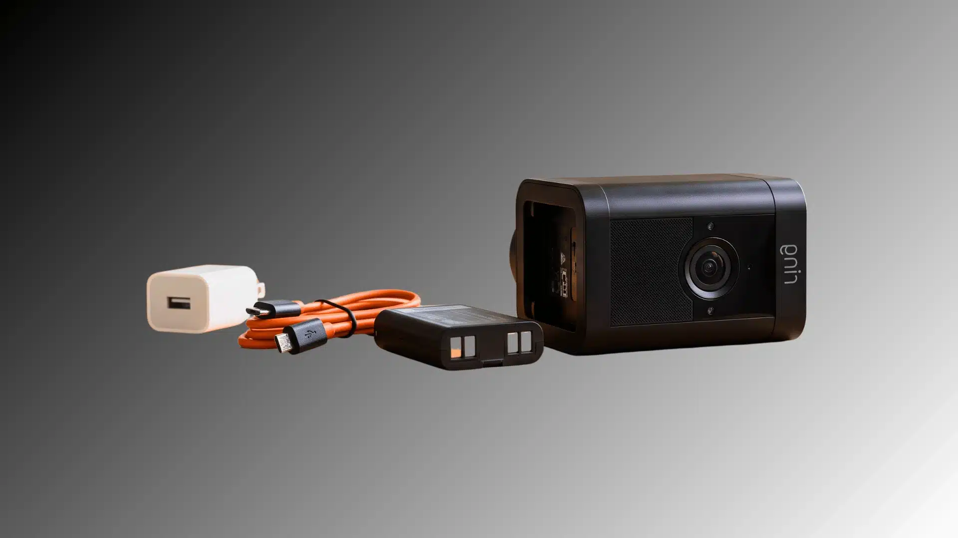 a black Ring camera with its battery, orange cable, and charger