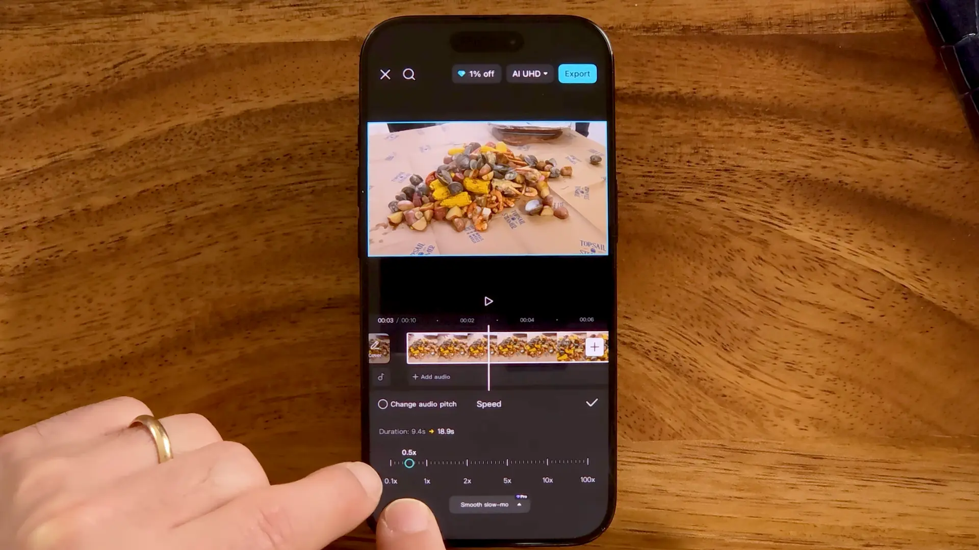 A hand adjusts speed settings to 0.5x in the CapCut video editing app on an iPhone placed on a wooden table.