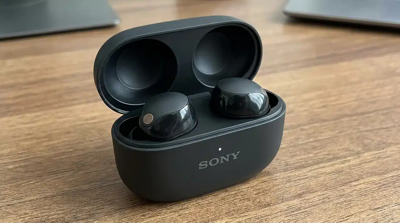 Sony wireless earbuds resting inside an open black charging case on a wooden desk.