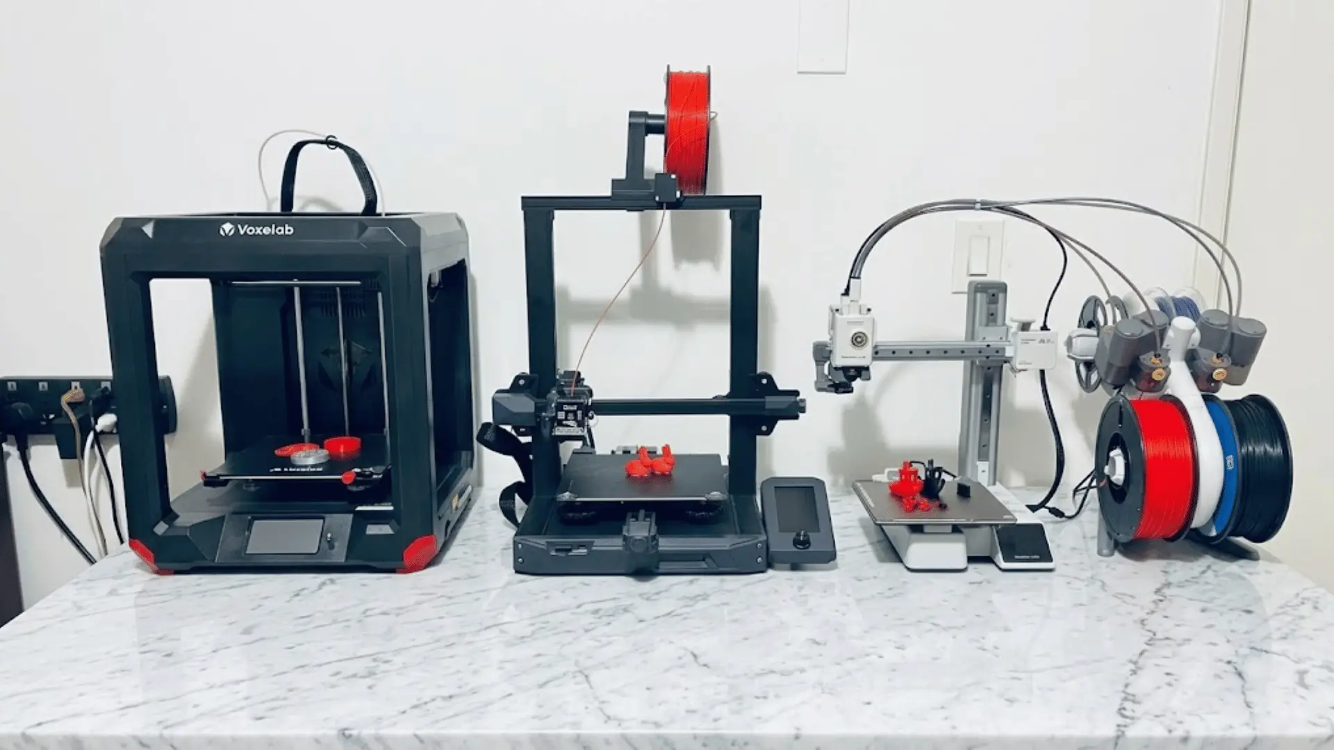 Three 3D printers on a table with filament spools, printed models, and multicolor filament system