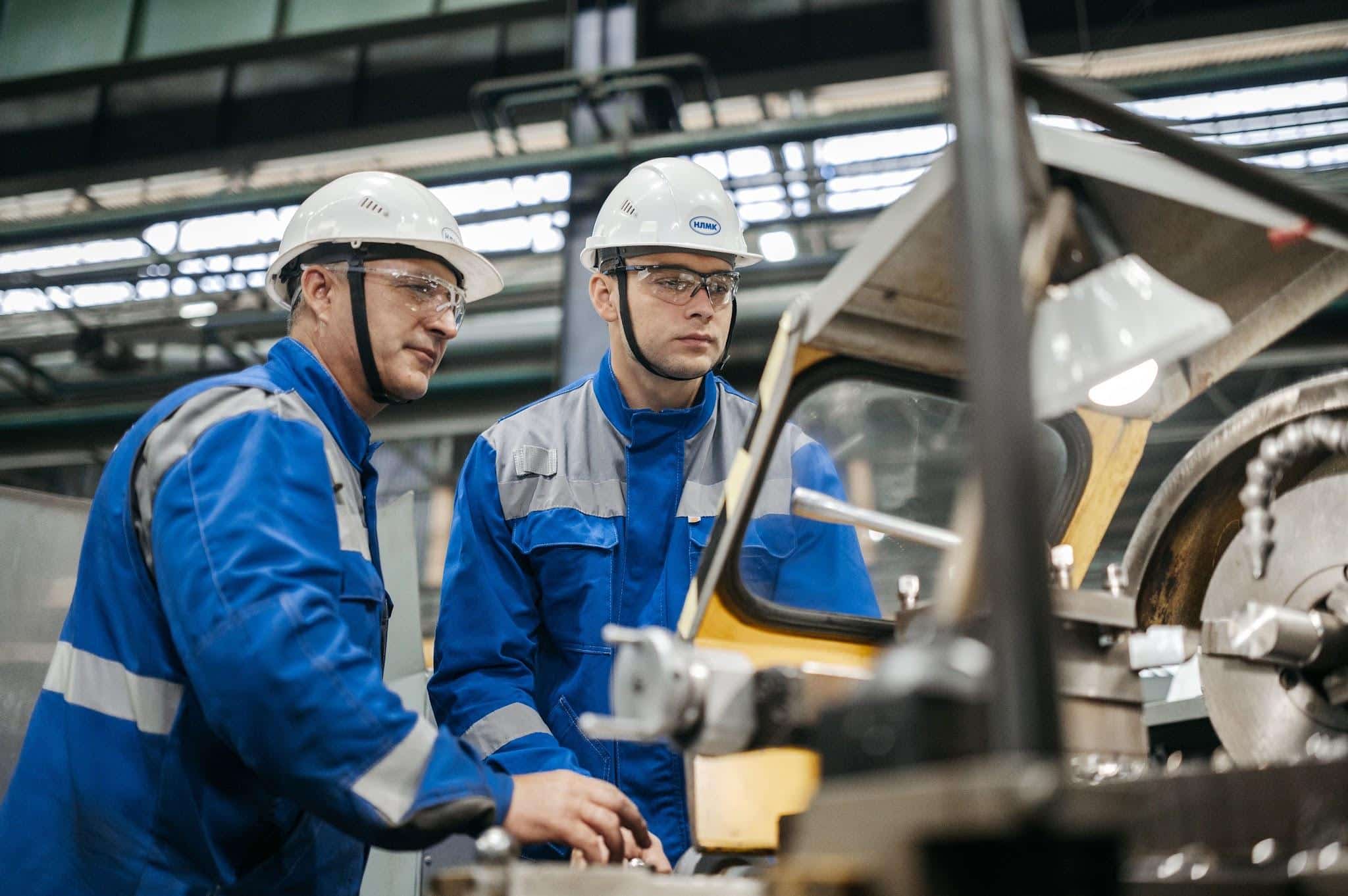 Two industrial workers in protective gear operate machinery.
