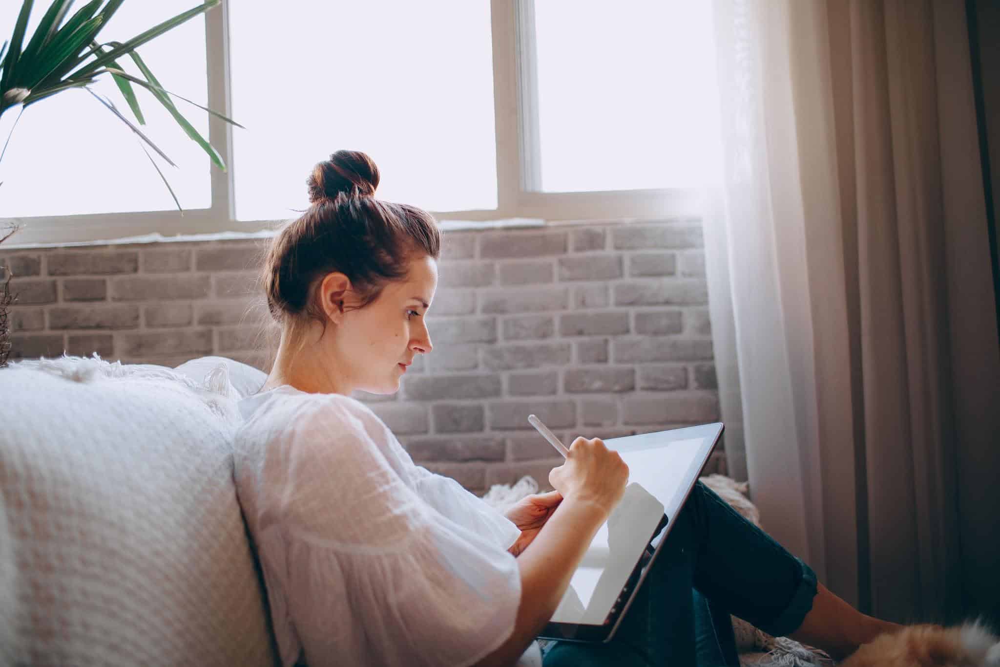 Woman sitting comfortably on a sofa using a tablet.