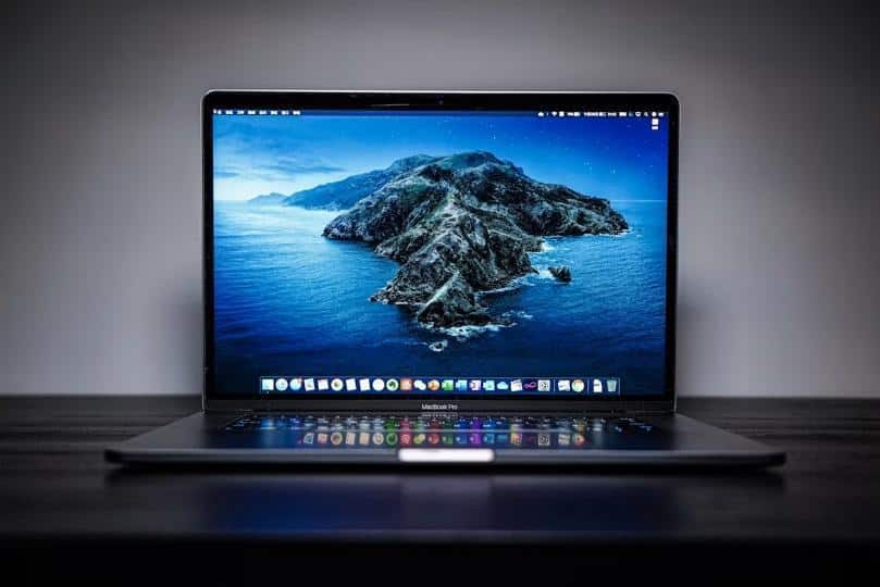 Open MacBook Pro on dark wooden desk displaying ocean island wallpaper