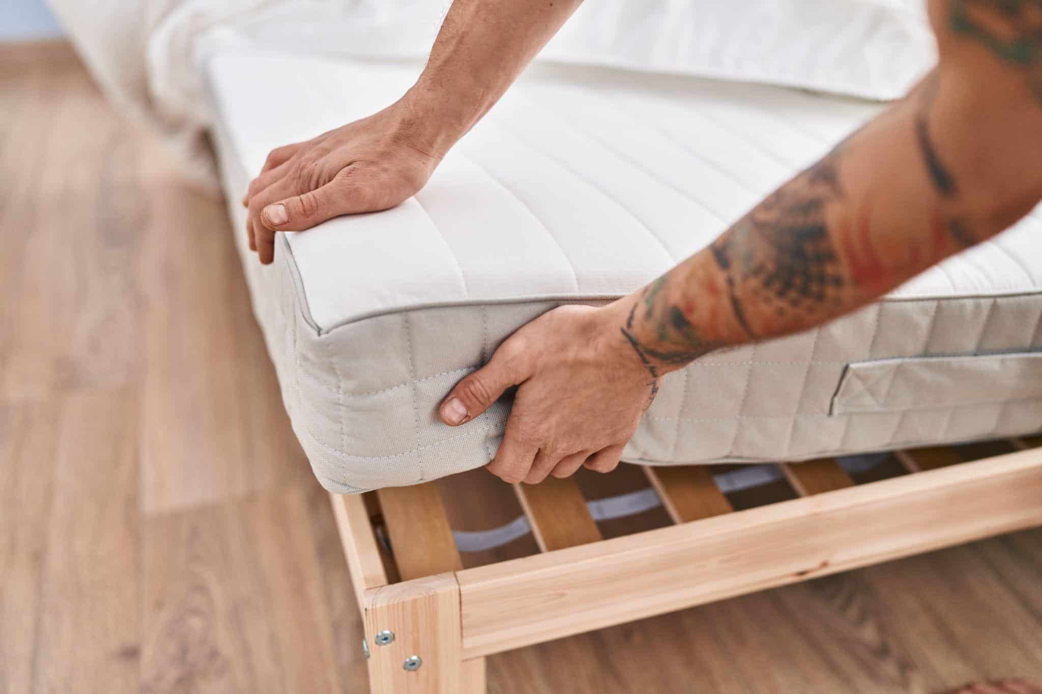 Hands adjusting white mattress on wooden bed frame in bright room