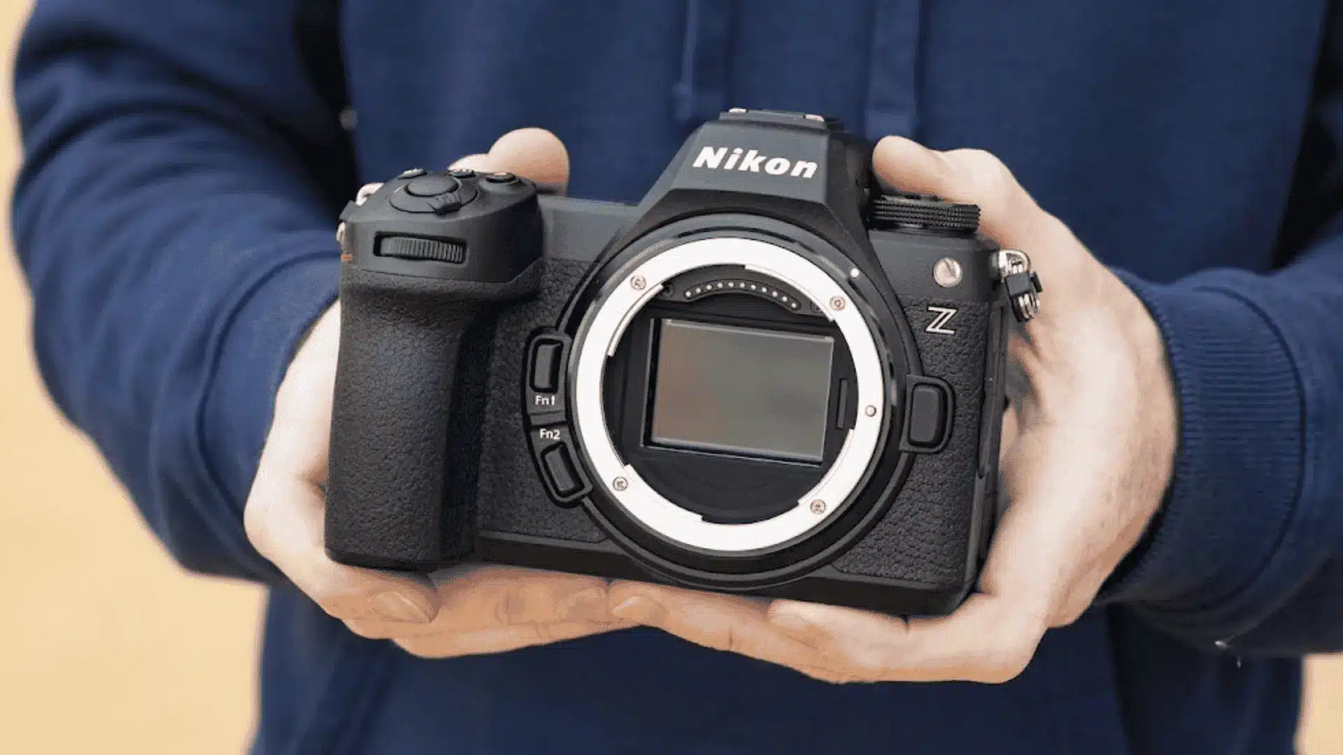 Hands holding a black Nikon Z series mirrorless camera body without a lens, revealing the camera sensor.