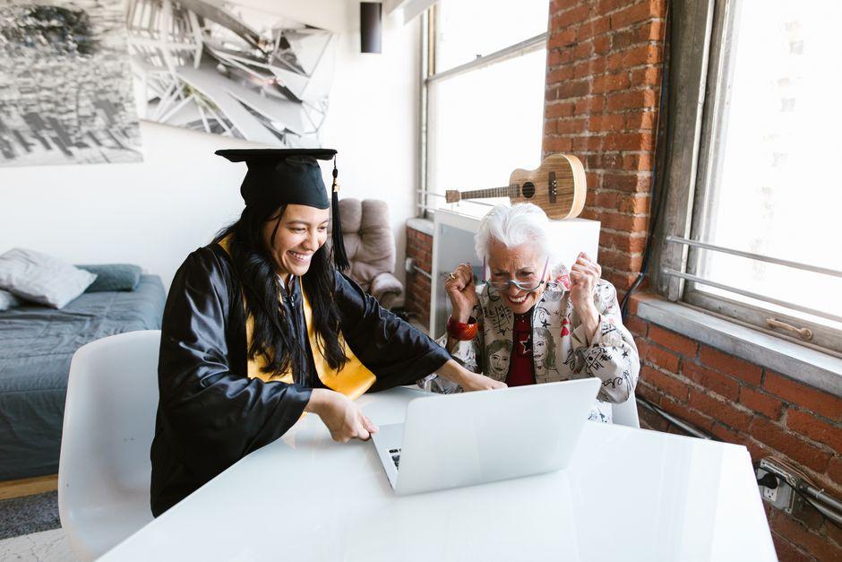 Graduate in cap and gown celebrating with elderly woman in industrial-style living room