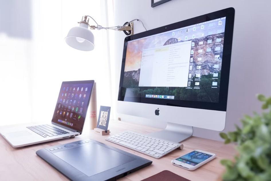 Workspace with Apple desktop and laptop, digital drawing tablet, and smartphone on wooden desk